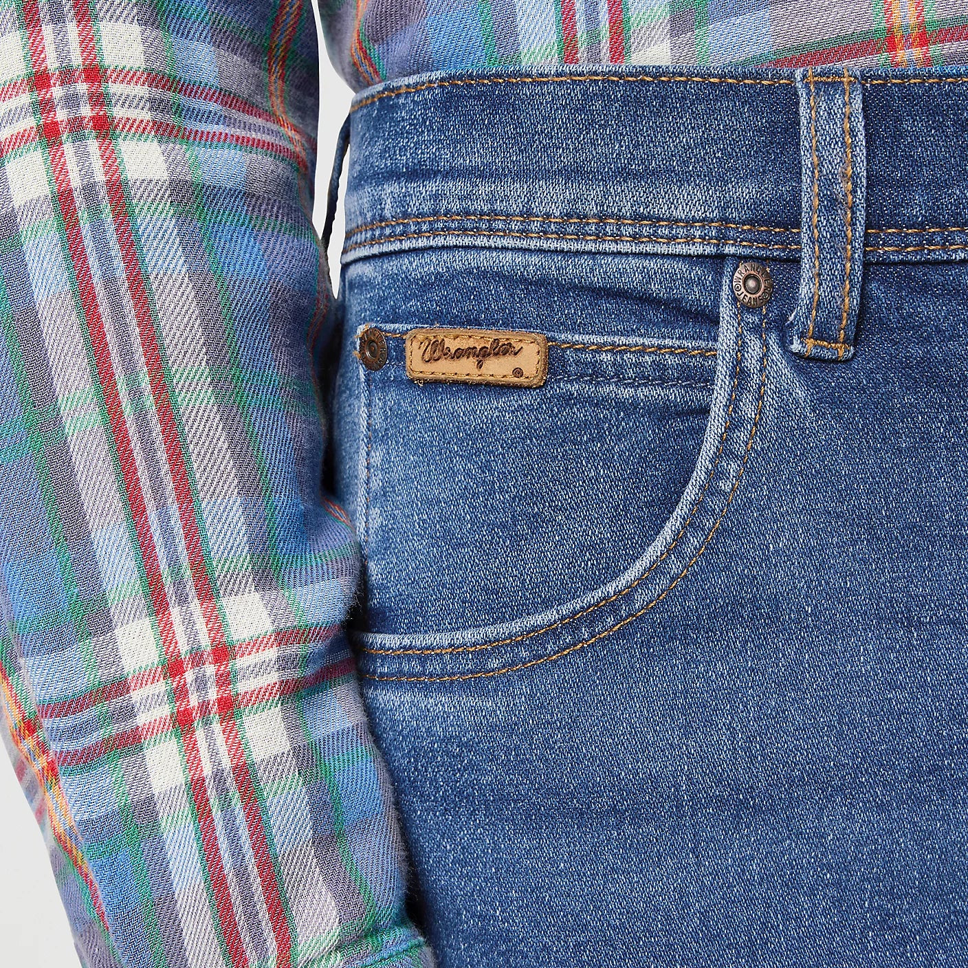 Close-up of blue jeans with a brand logo and a plaid shirt sleeve.
