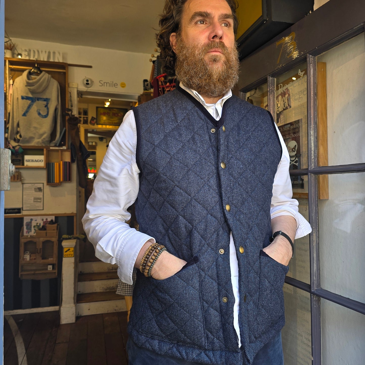 Man wearing a blue quilted vest and white shirt in an indoor setting with shelves and boxes.
