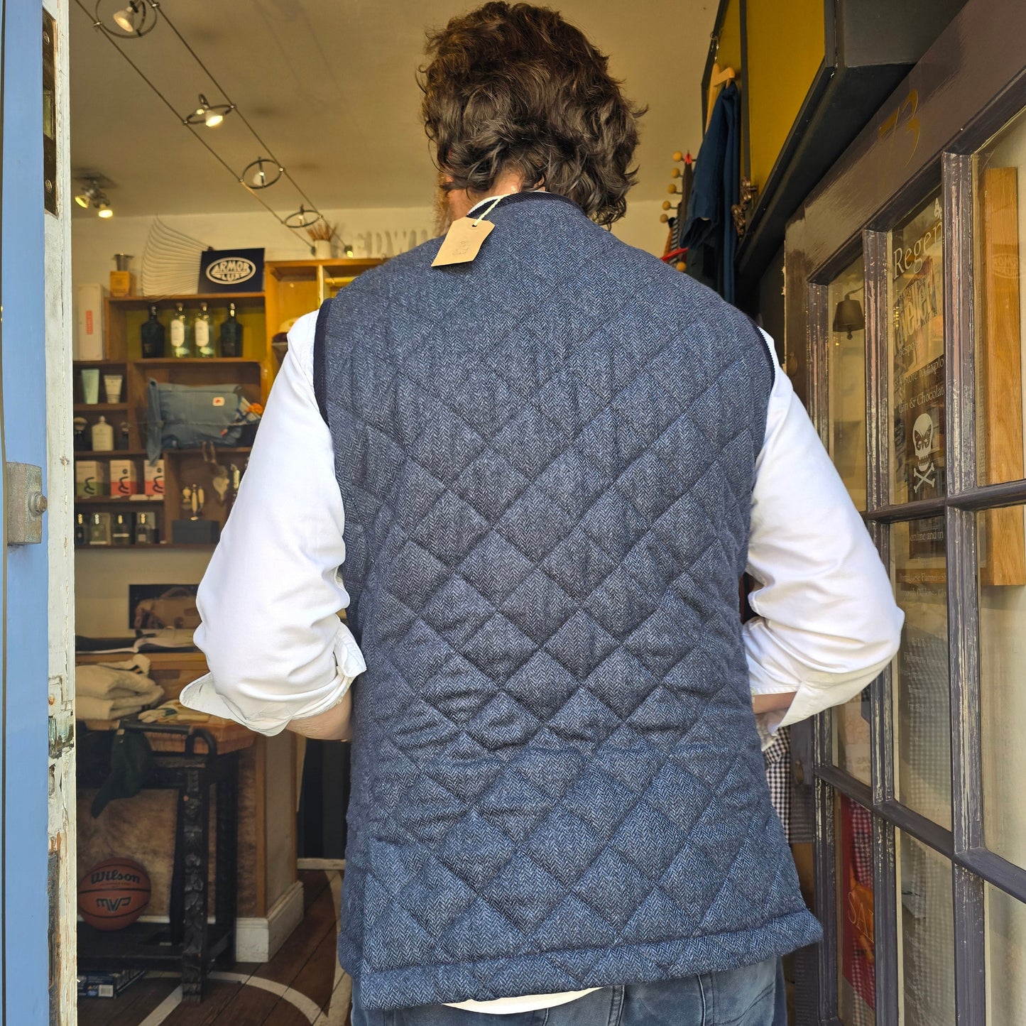 Person wearing a quilted gray vest in an indoor setting with shelves and decor.