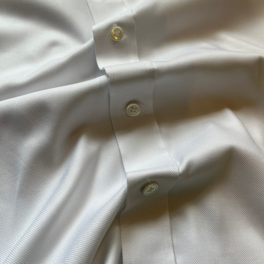 Close-up of a white textured button-down shirt showing the collarless placket, button details, and fabric texture.