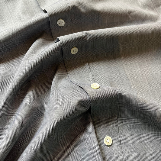Close-up of a gray plaid button-down shirt fabric with cream-colored buttons, showing the texture and weave details.