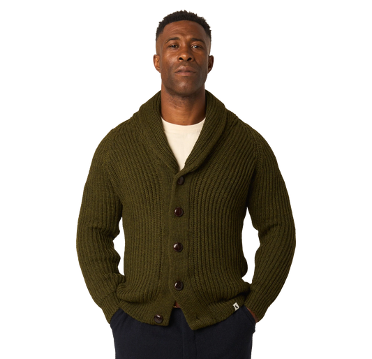 A man wearing an olive green ribbed knit cardigan with a shawl collar and dark buttons, layered over a cream t-shirt and dark pants, against a plain white background.