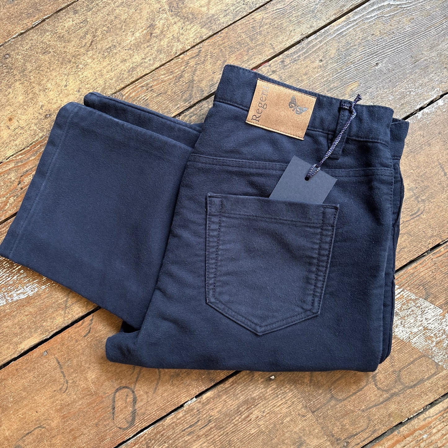 Folded navy blue jeans with a tag on a wooden surface