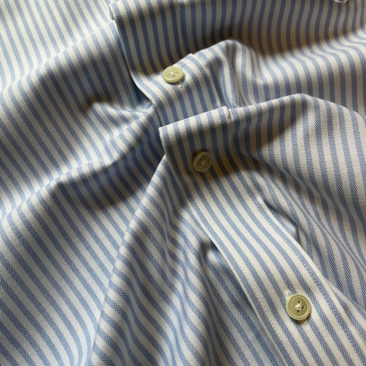 Close-up of a light blue and white striped shirt fabric with three light green buttons.