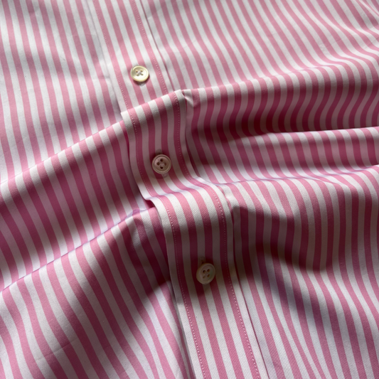 Close-up of a pink and white vertically striped button-down shirt fabric, showing the texture and three buttons on the placket.