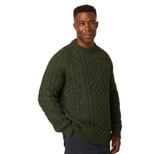 A man wearing a dark olive green cable-knit sweater, standing against a solid white background.