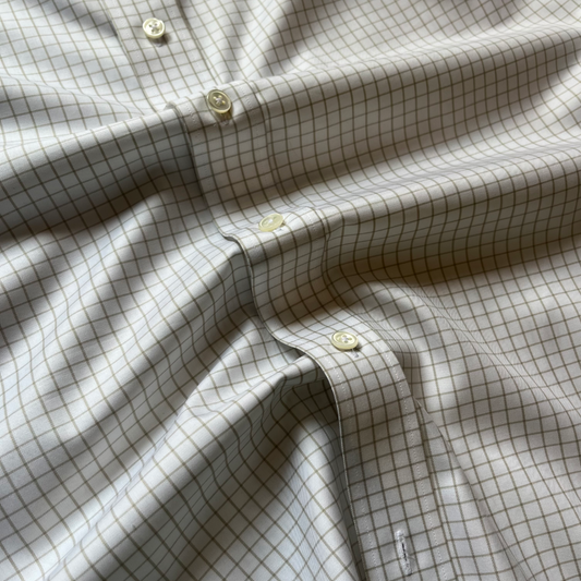 A close-up of a light beige or off-white button-up shirt with a fine brown grid check pattern and cream-colored buttons, shown with soft folds.