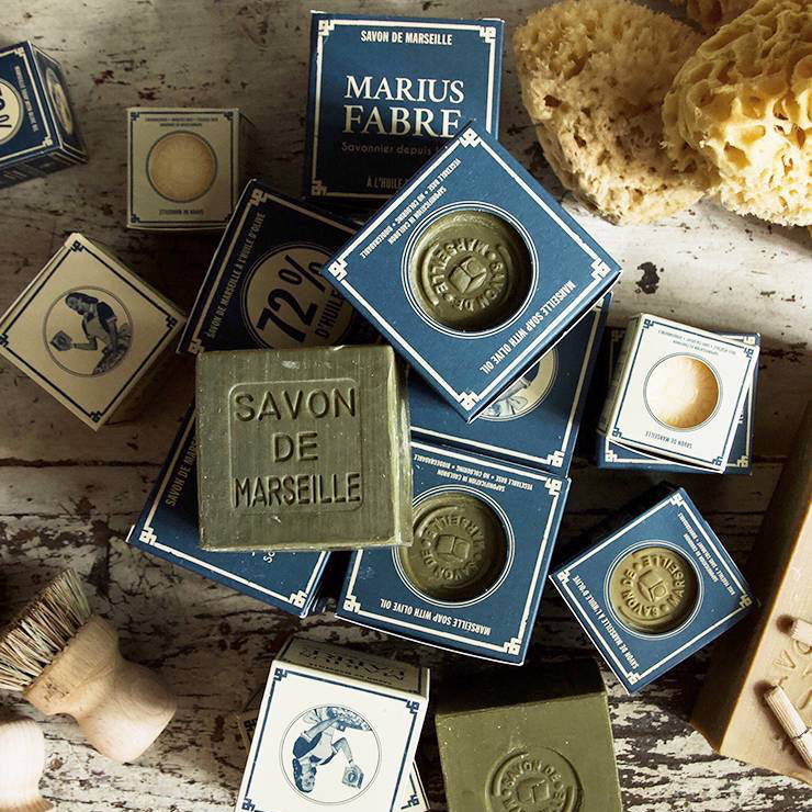 Marius Fabre Marseille soap bars and packaging on a rustic wooden surface with sponges and a brush.