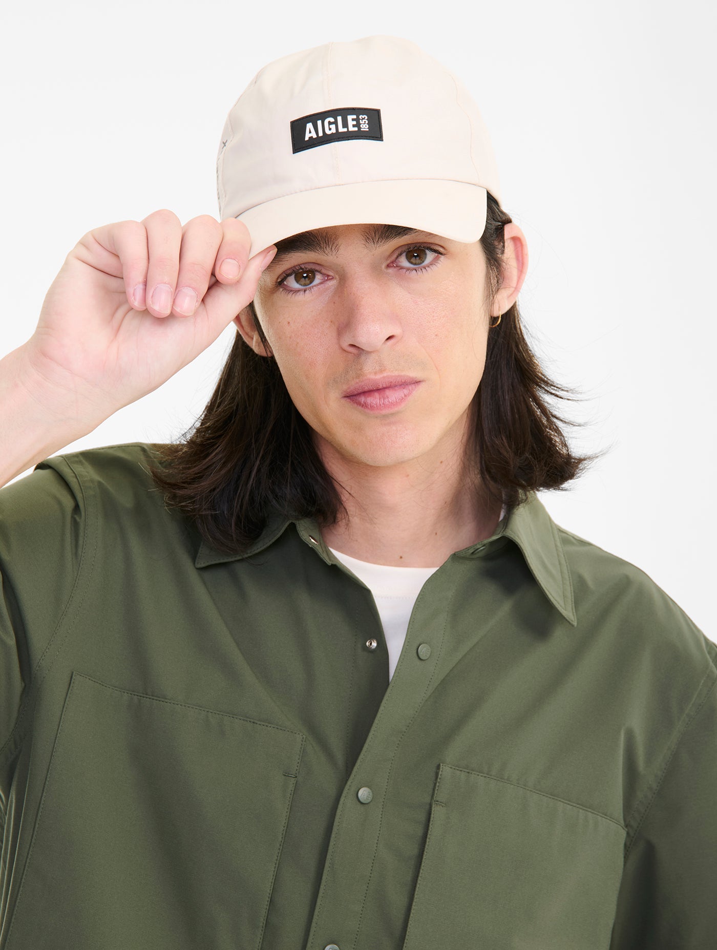 Person wearing a beige cap with 'Aigle' logo and a green shirt on a white background