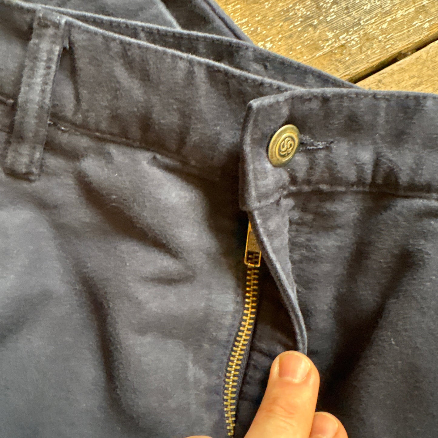 Close-up of a dark denim jacket with a hand zipping it up on a wooden surface.
