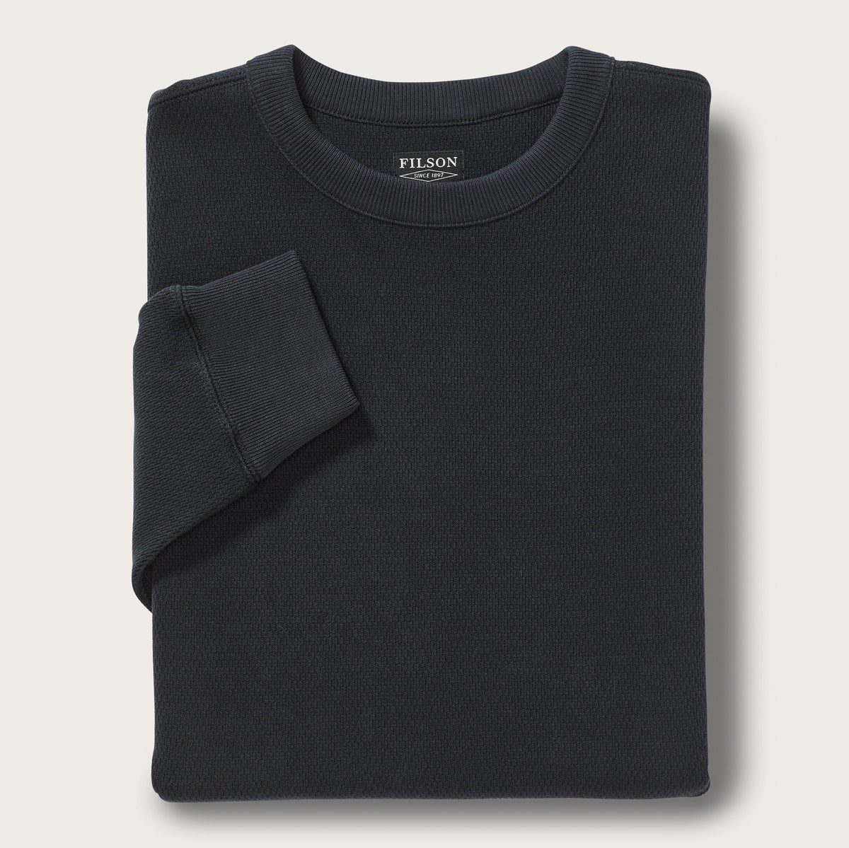 Folded black sweater with Filson logo on a light gray background
