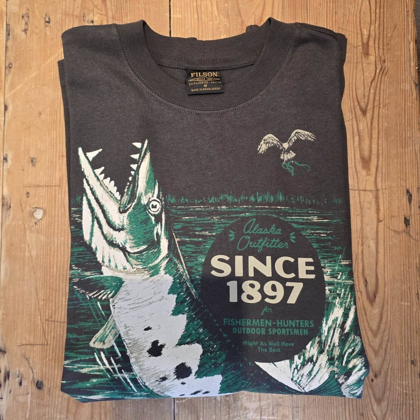 Dark gray t-shirt with graphic design and text on a wooden surface