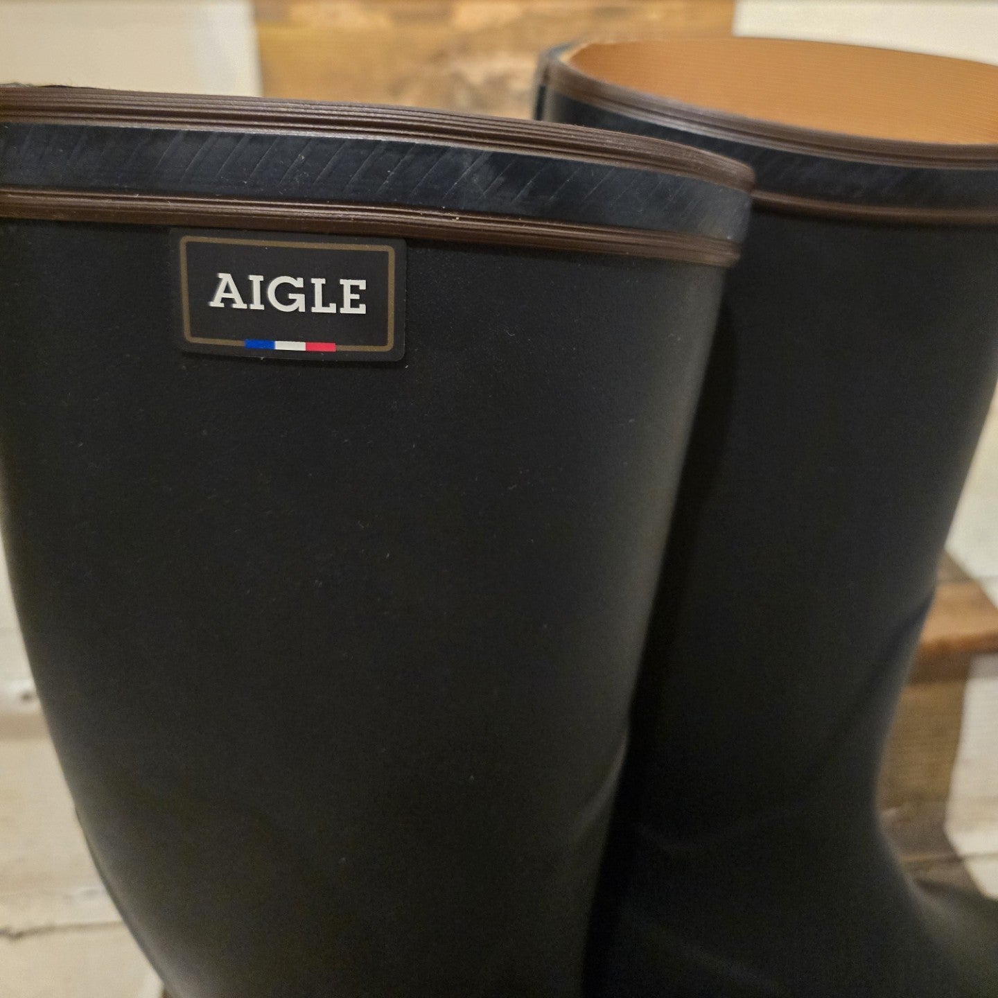 Black rain boots with Aigle logo on a blurred indoor background