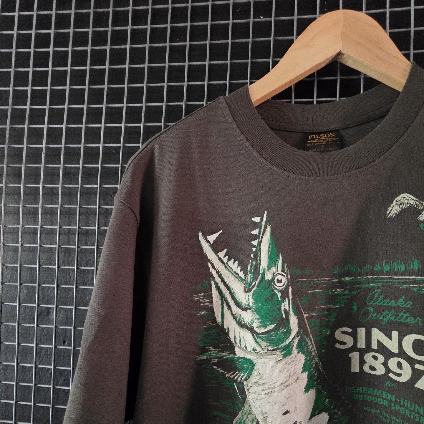 T-shirt with fish graphic and text on a hanger against a tiled wall