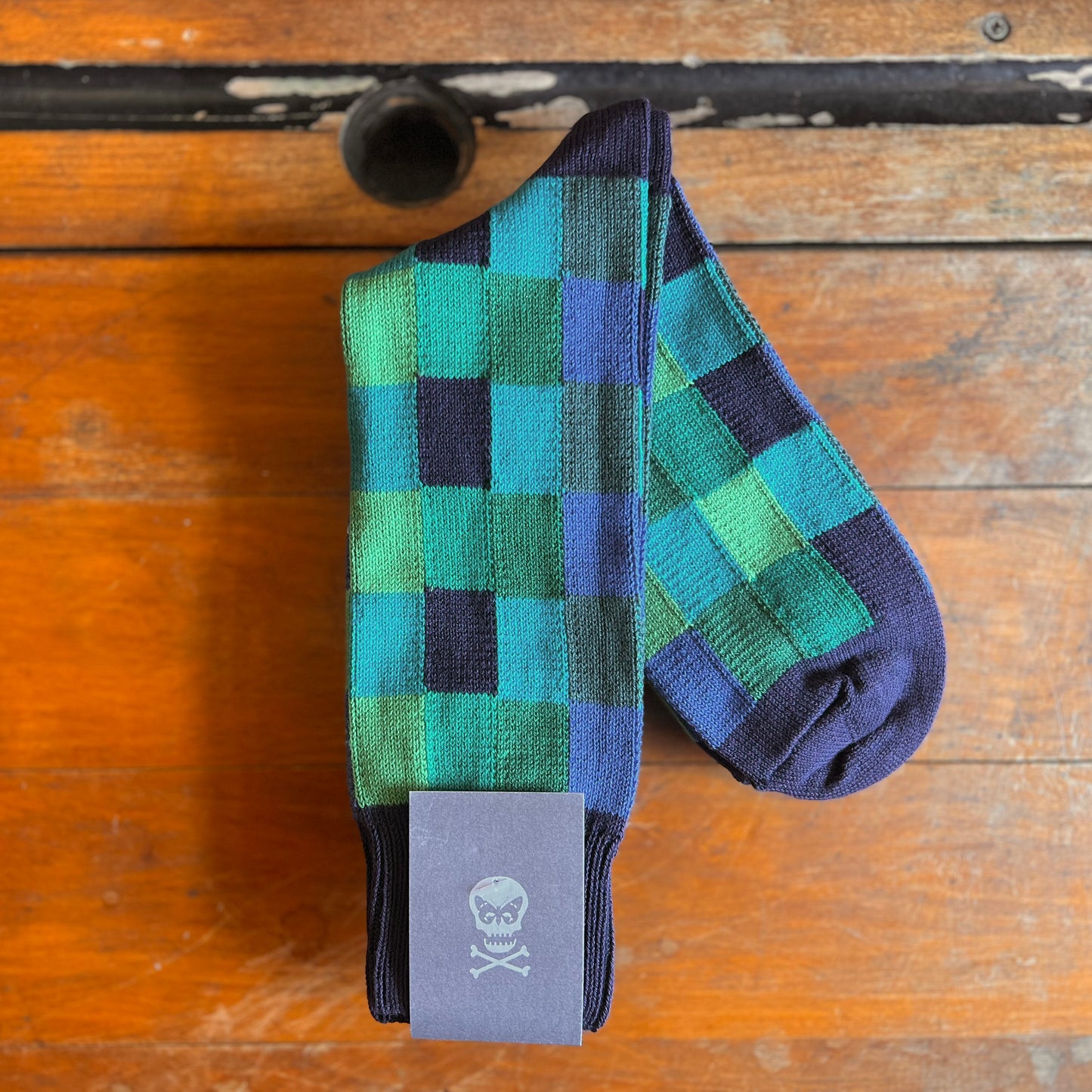 Turquoise Multi checked socks on a wooden background. They have lime, azure, navy and light purple areas.