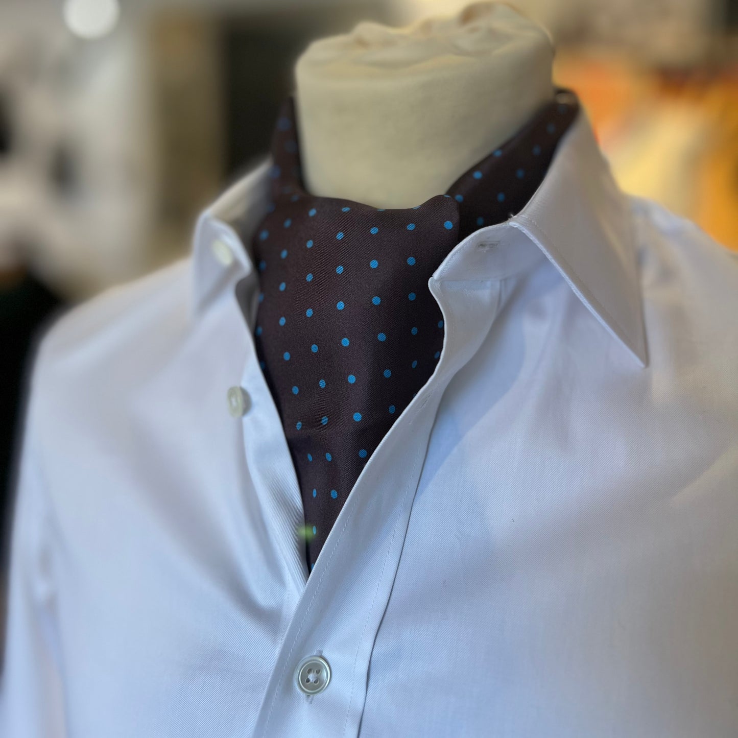 A brown tootal scarf with blue dots tied in a cravat style on a mannequin