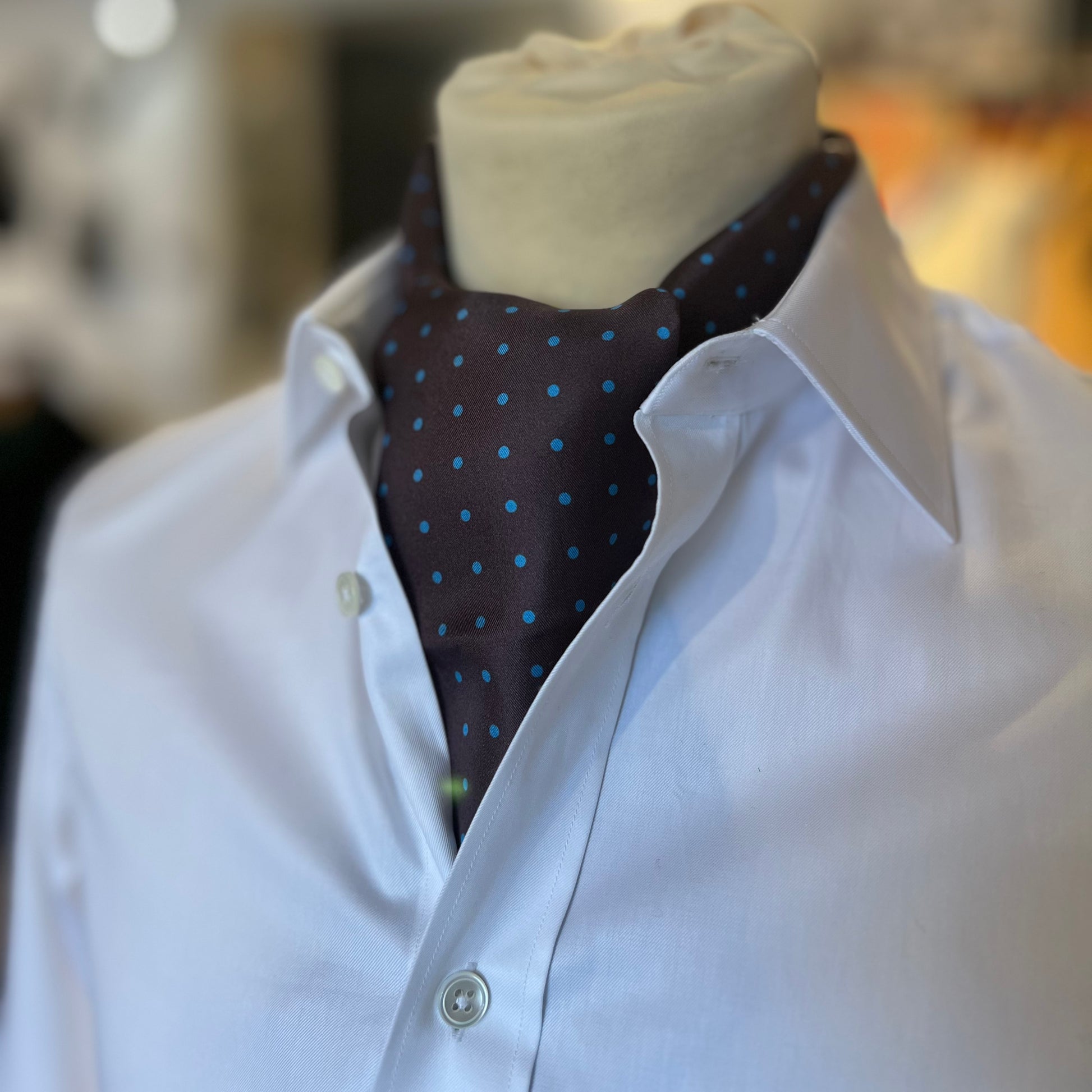 A brown tootal scarf with blue dots tied in a cravat style on a mannequin