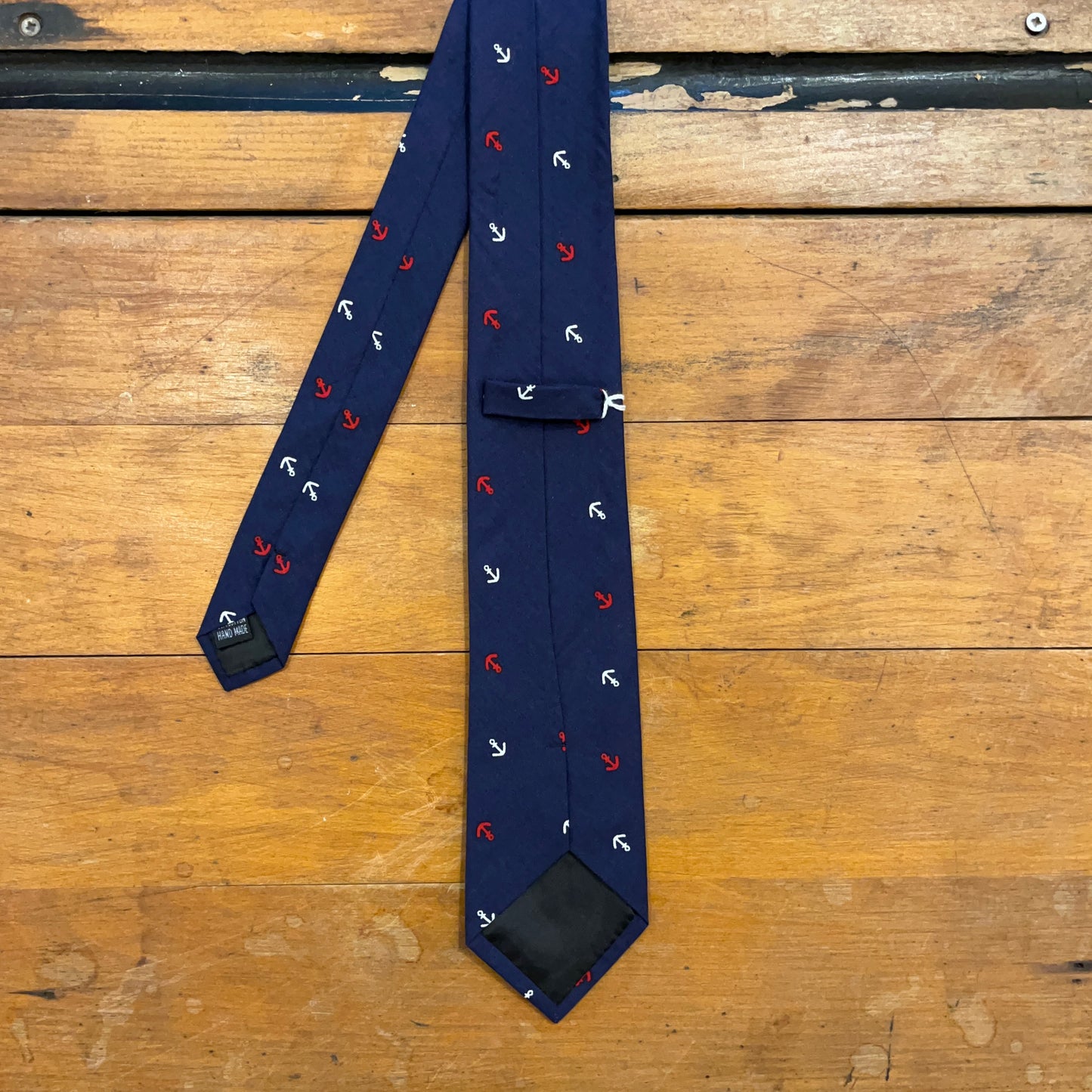 Reverse of navy cotton tie with anchor pattern on wooden boards