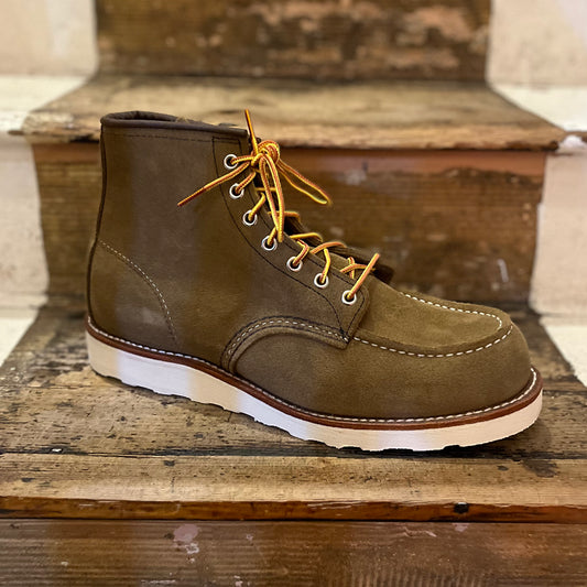 A brown olive mohave suede Red Wing classic moc-toe boot with white traction tread sole and leather footbed, displayed on a wooden step.