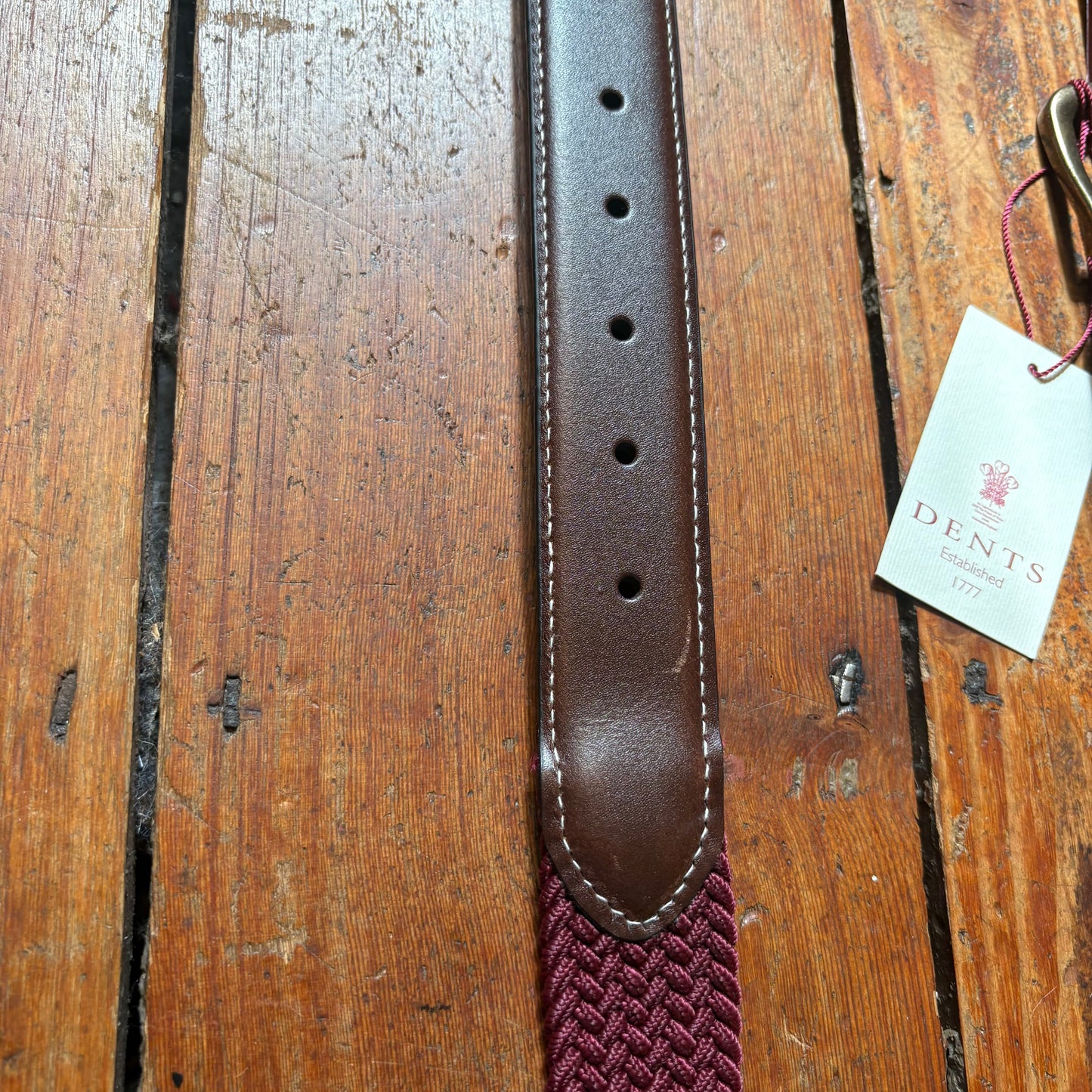 Brown leather belt with a maroon woven strap on a wooden surface, featuring a Dents label.
