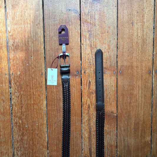 Two black leather belts with a Dents tag on a wooden surface