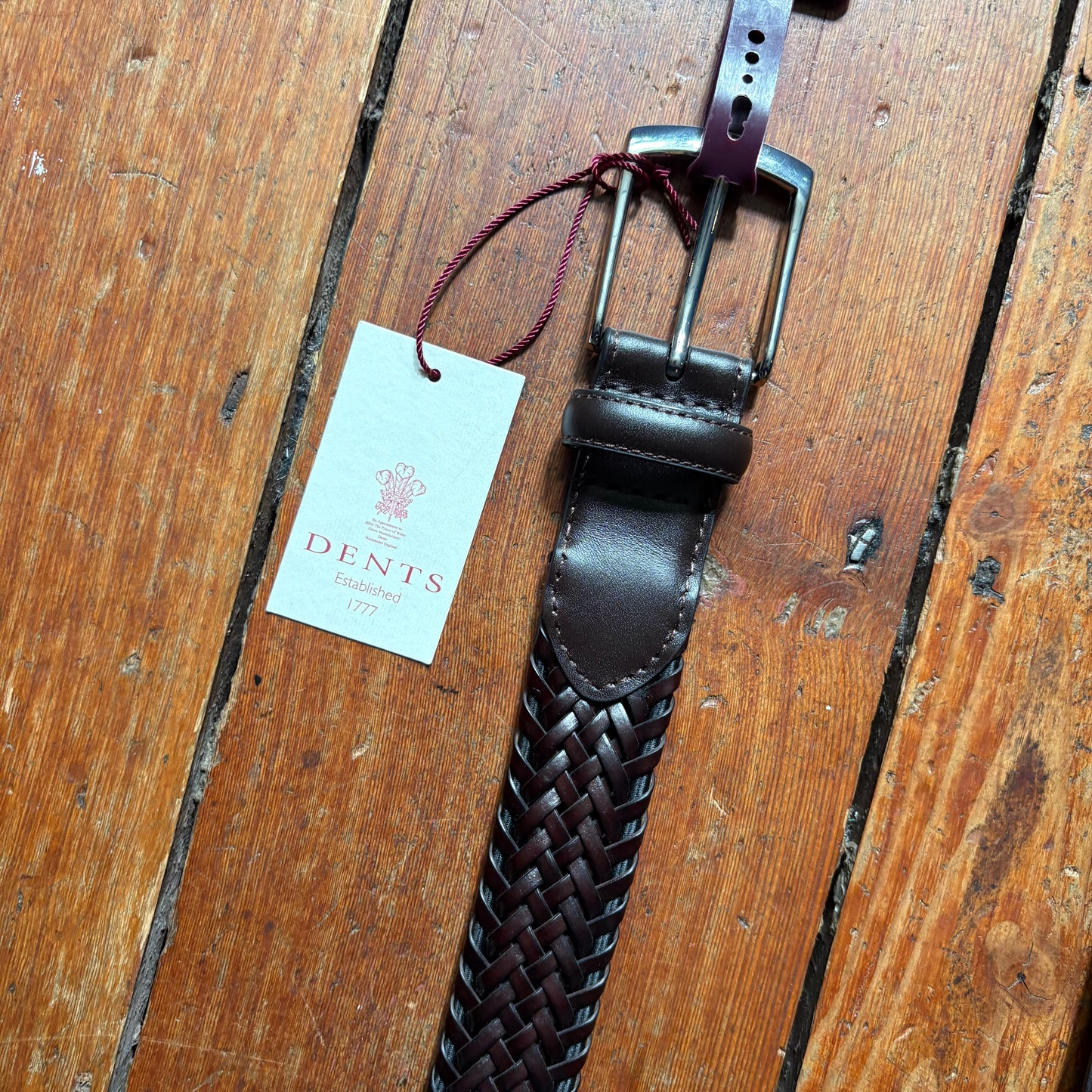 Brown leather belt with woven pattern and Dents tag on wooden surface