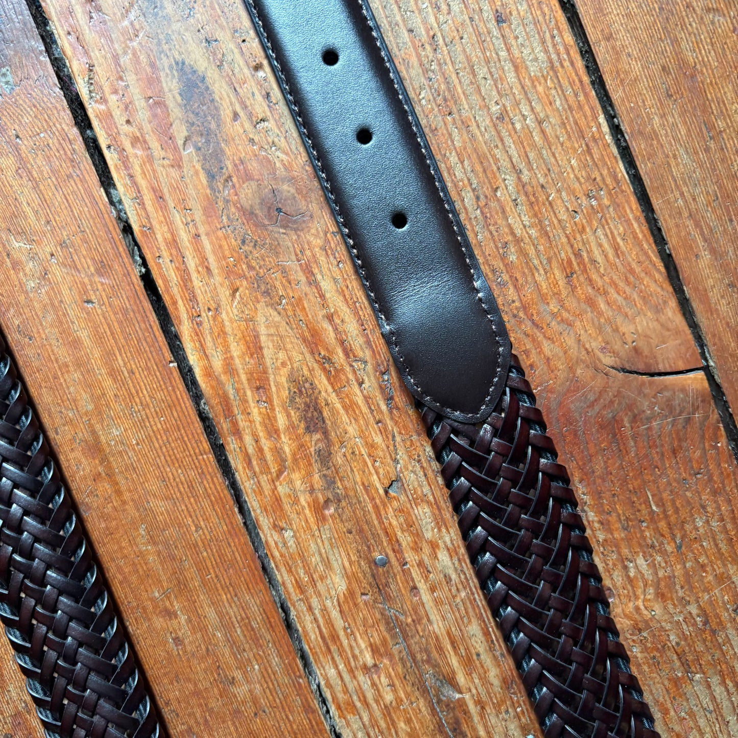 Black leather belt with woven pattern on a wooden surface