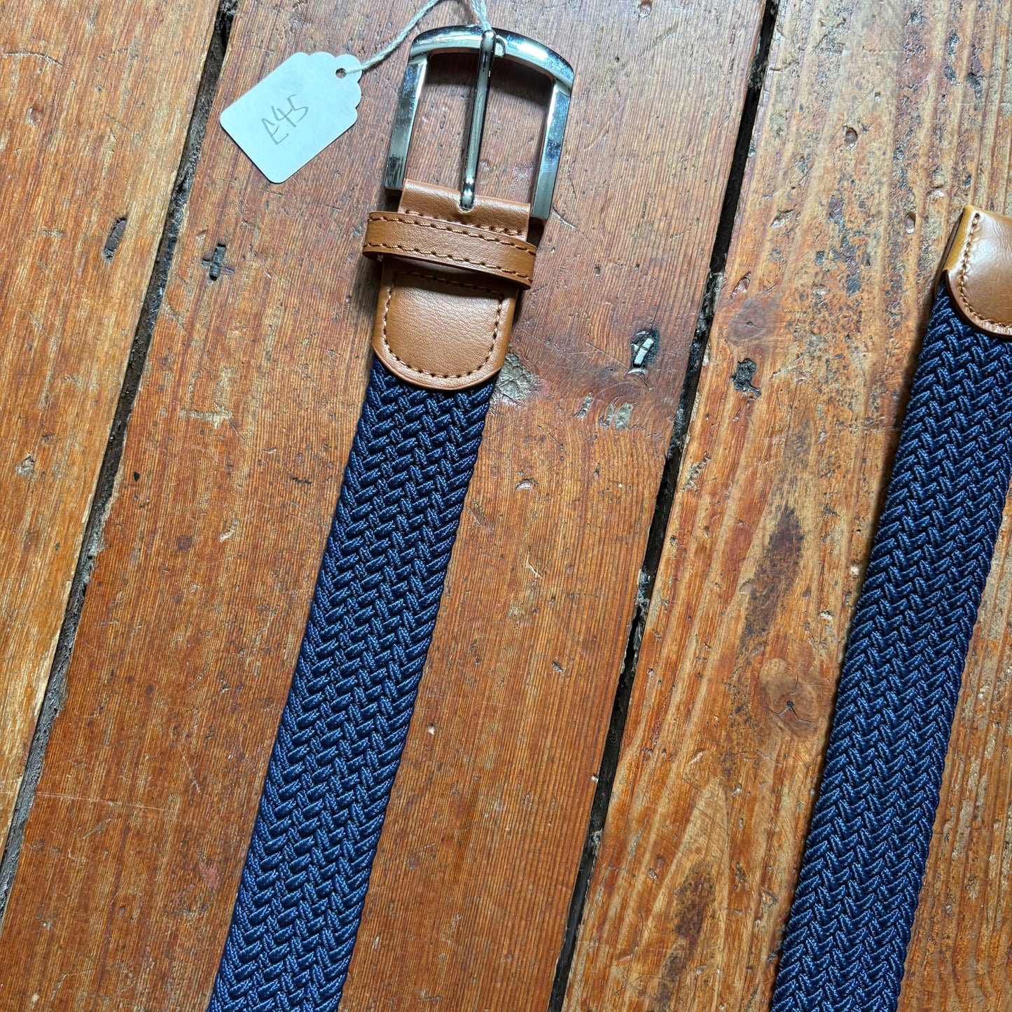 Blue woven belt with brown leather buckle on a wooden surface
