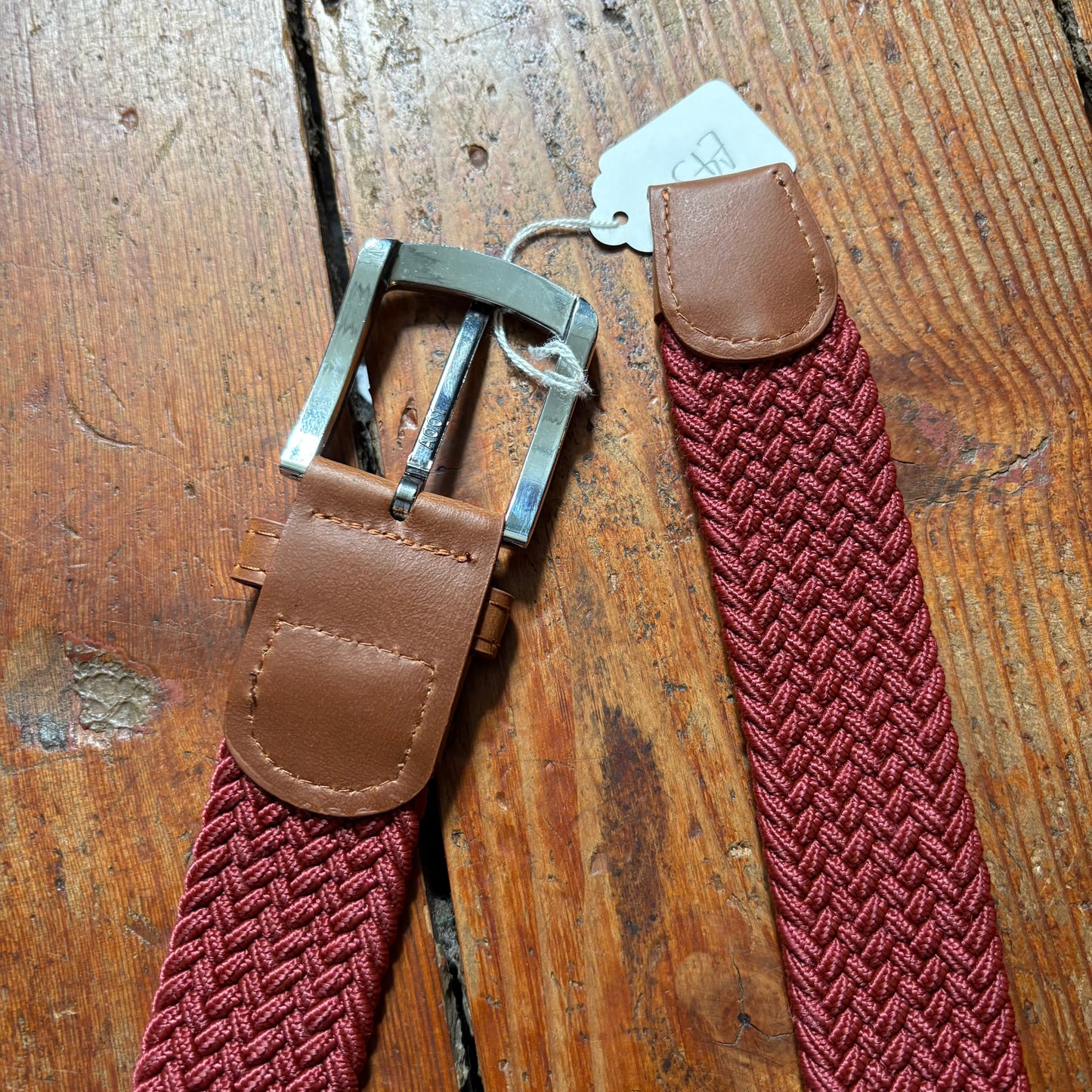 Red woven belt with brown leather straps on a wooden surface