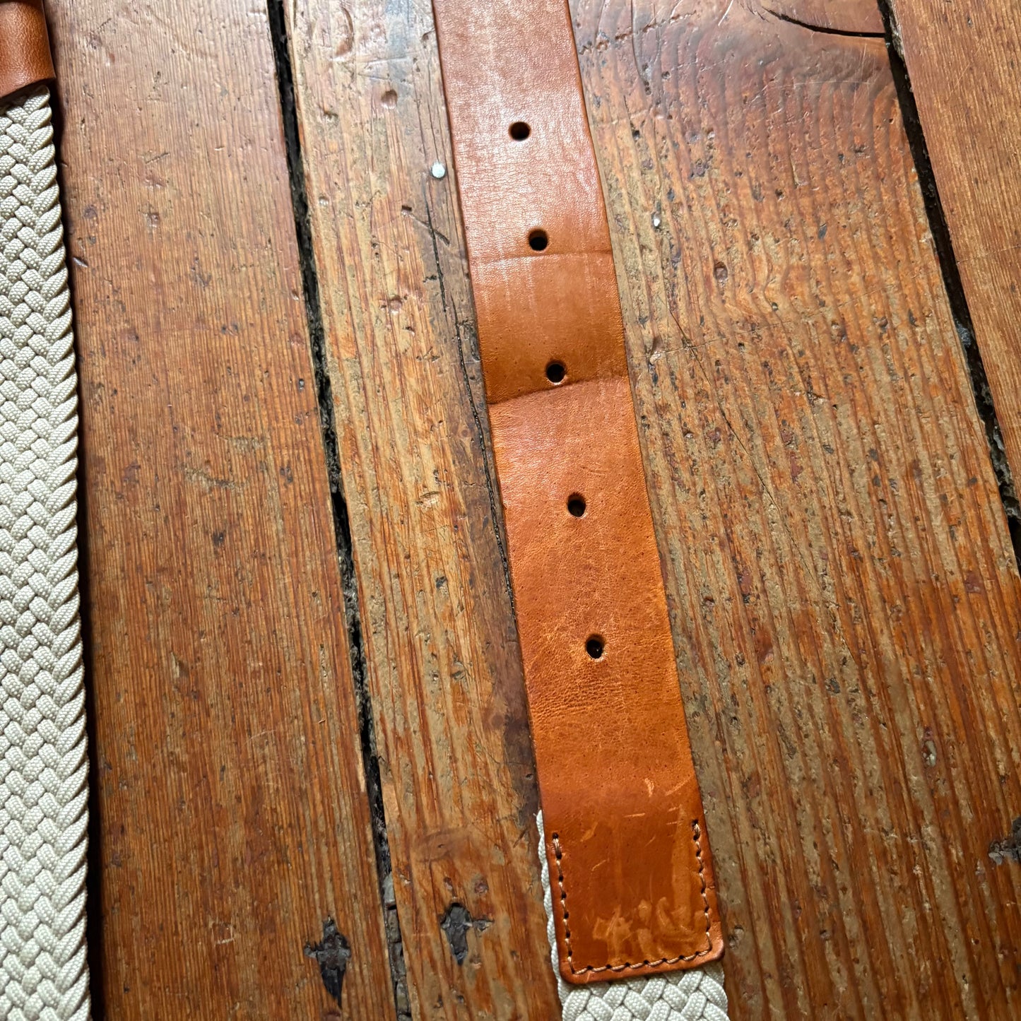 Brown leather belt with rope ends on a wooden surface