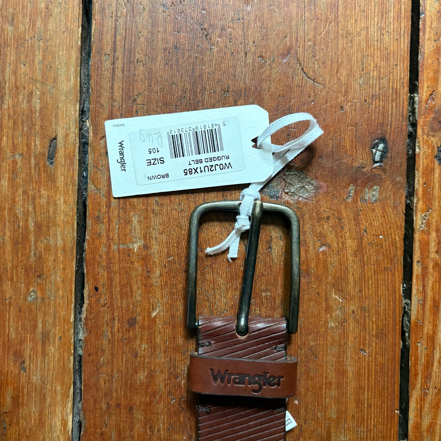 Brown belt with metal buckle and Wrangler logo on a wooden surface