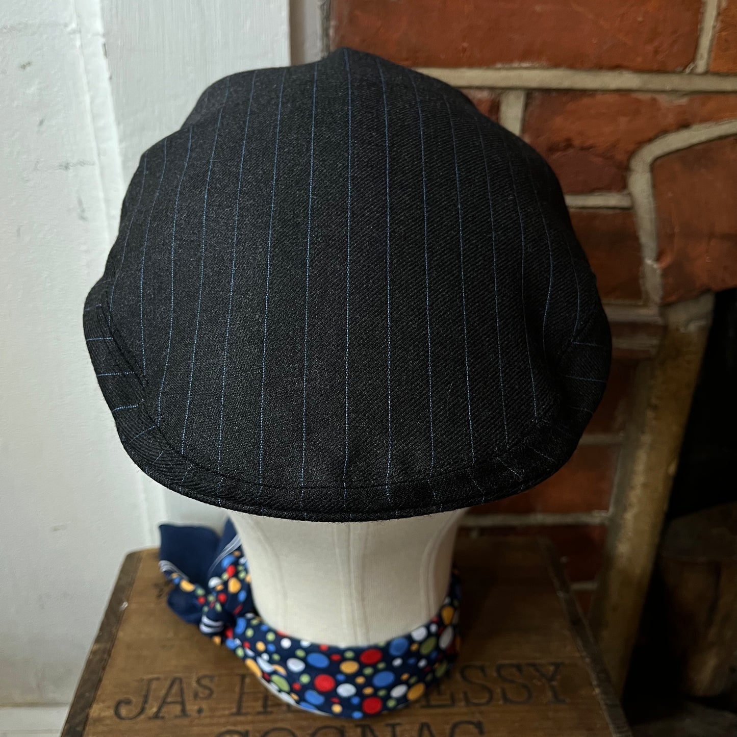 Black pinstripe cap on a mannequin head with a colorful bandana against a brick wall.