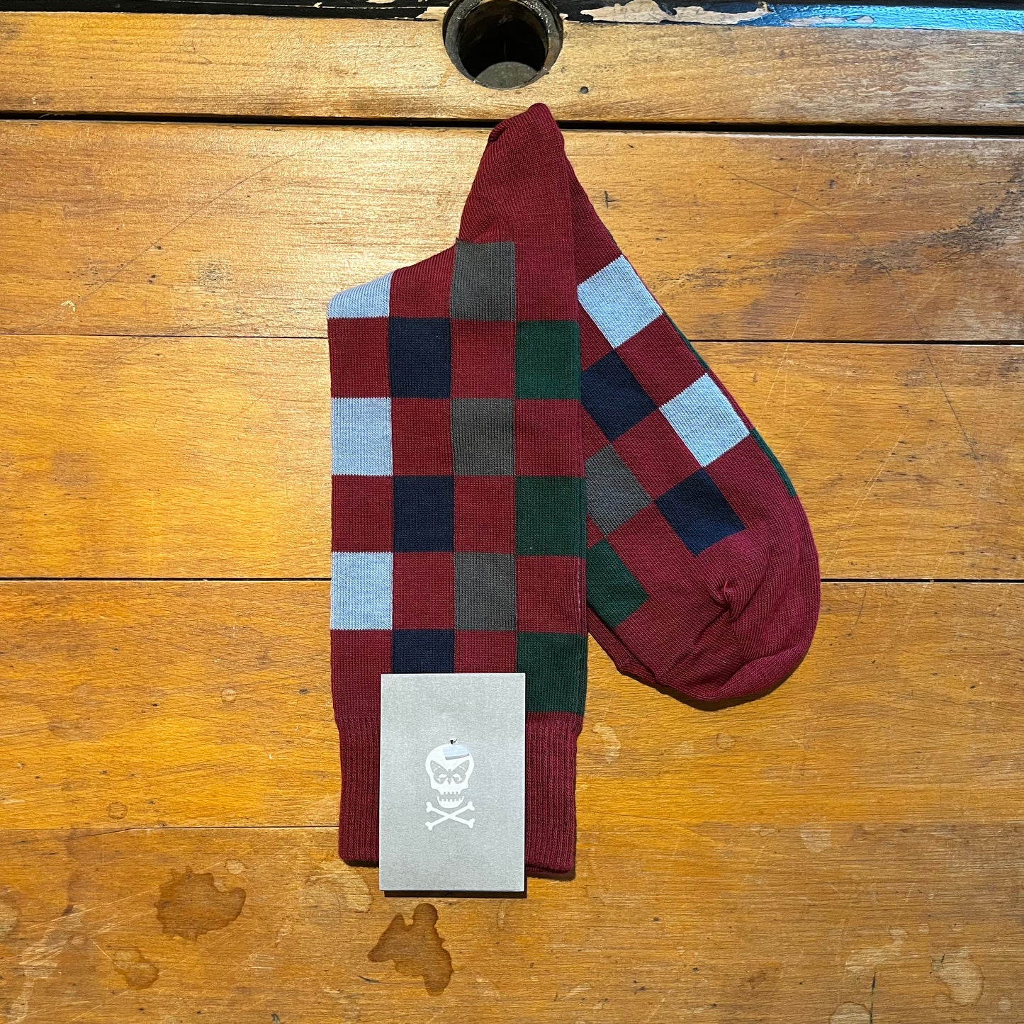 burgundy and multi checkered socks with a box on a wooden surface