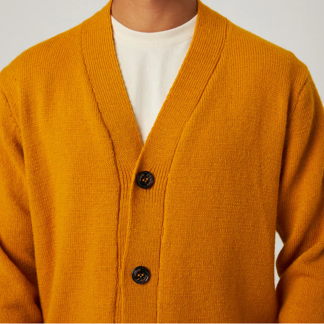 Man wearing a mustard yellow cardigan over a white shirt on a plain background