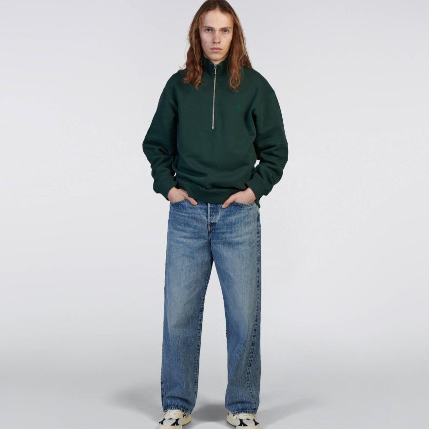 Person wearing a green sweatshirt and blue jeans on a white background