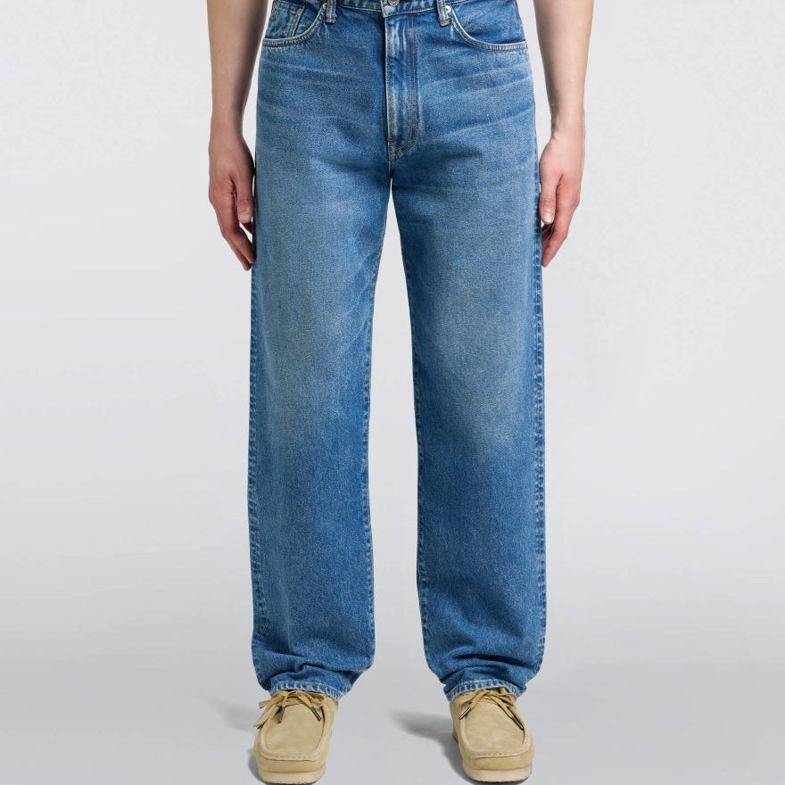 Person wearing blue jeans and beige shoes on a white background