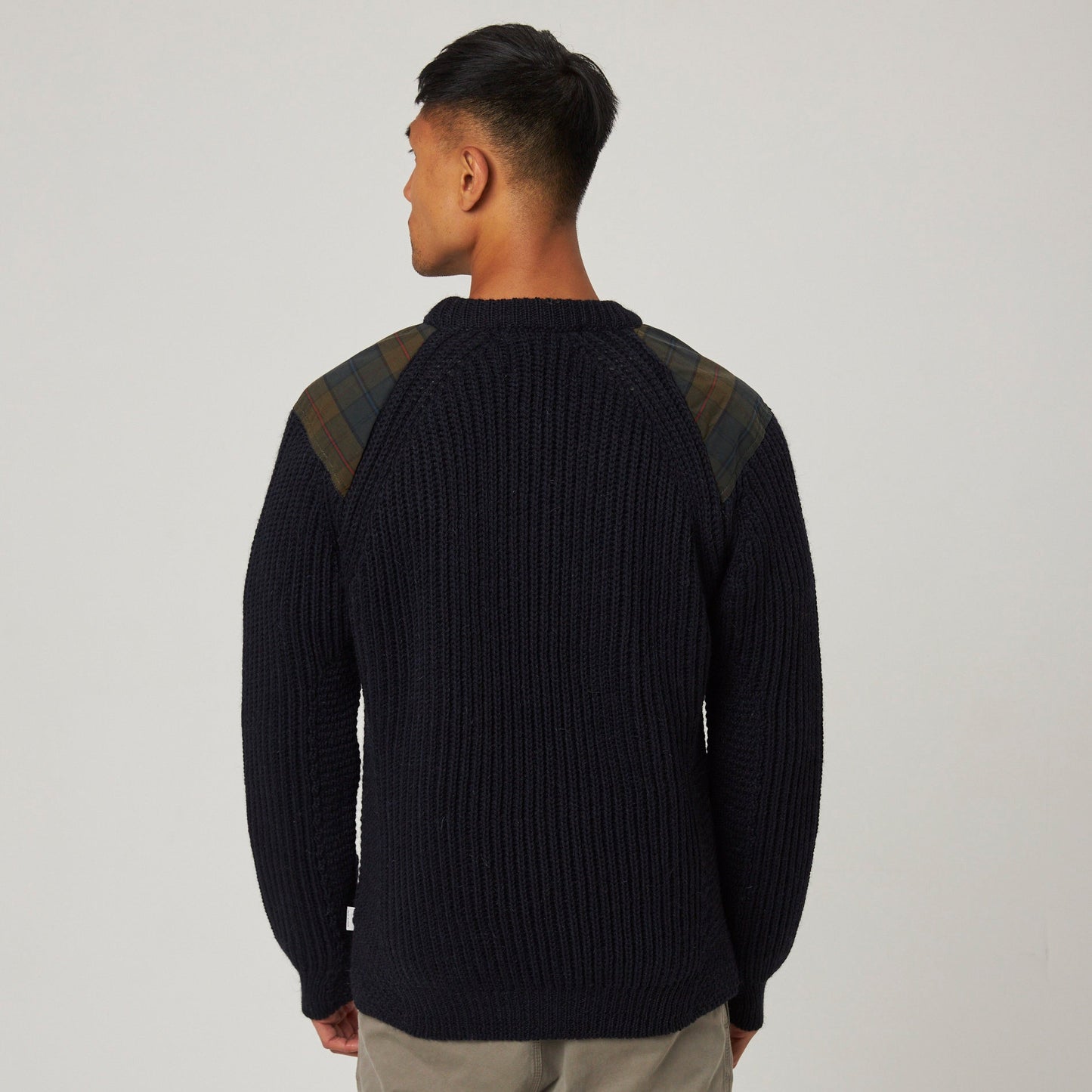 Person wearing a black sweater with green accents on a plain background