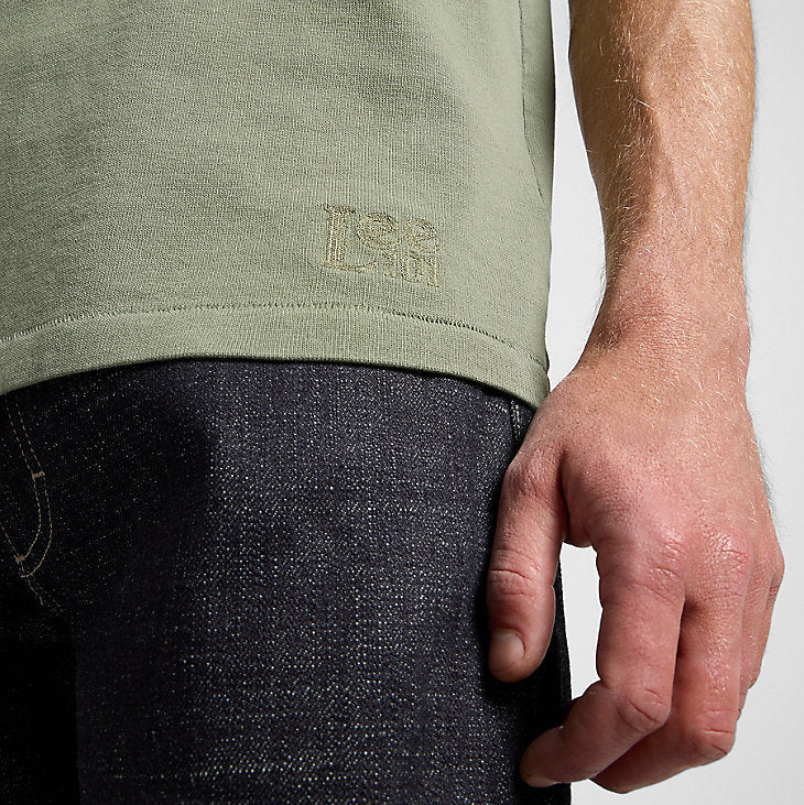 Person wearing a green t-shirt with a logo on a plain background