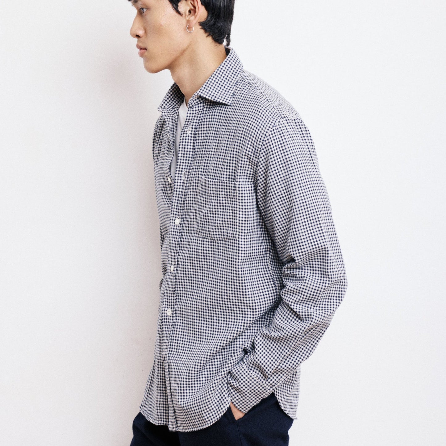 Man wearing a checkered shirt and dark pants against a white background