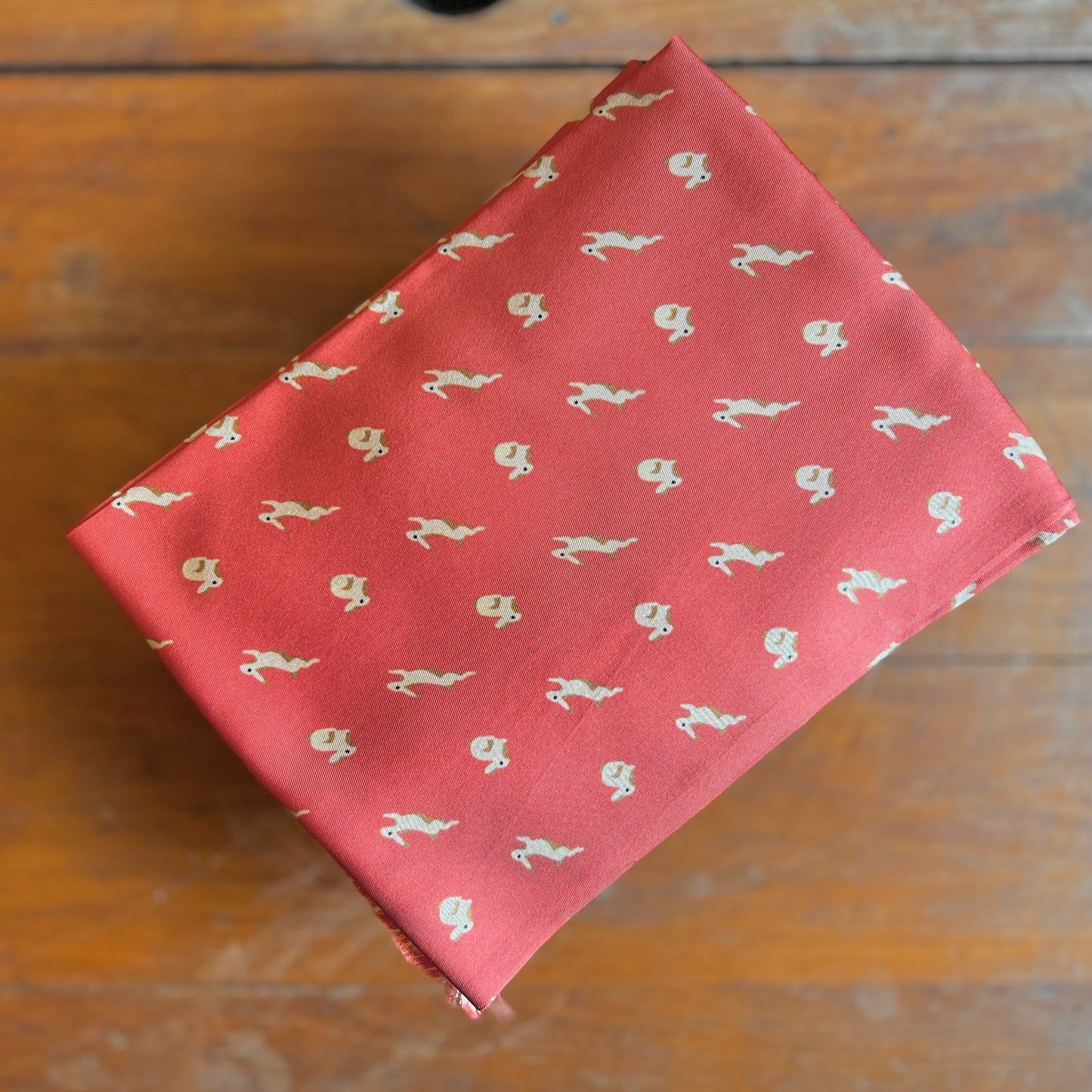A folded, orange tootal scarf with a printed pattern of bunny rabbits against a wooden backdrop.