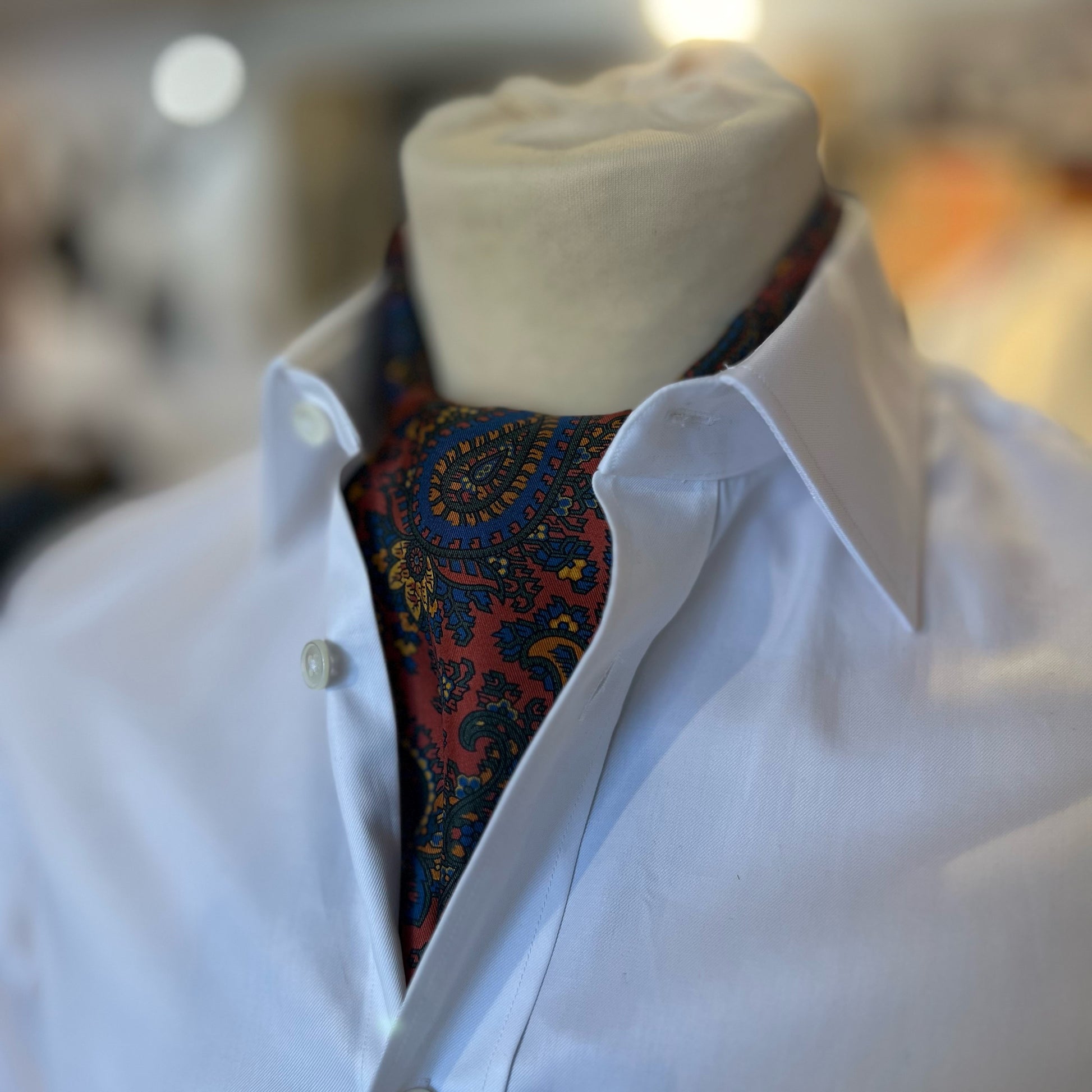 A red tootal scarf with a paisley pattern tied in a cravat style around the neck of a mannequin