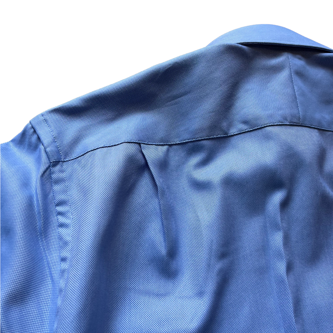 Close-up of the back of a blue textured button-up shirt, showing the collar seam, shoulder stitching, and fine woven fabric texture