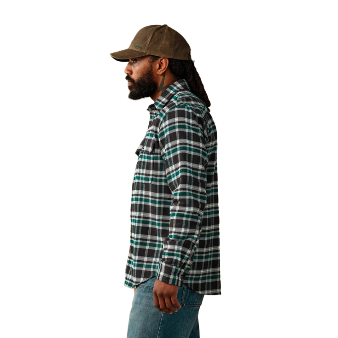 A man shown in profile wearing a brown cap, a black and green plaid flannel shirt, and blue jeans against a plain white background.