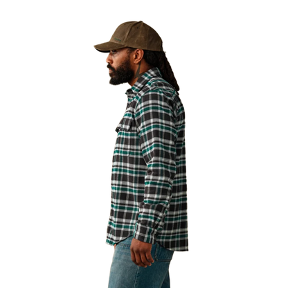 A man shown in profile wearing a brown cap, a black and green plaid flannel shirt, and blue jeans against a plain white background.