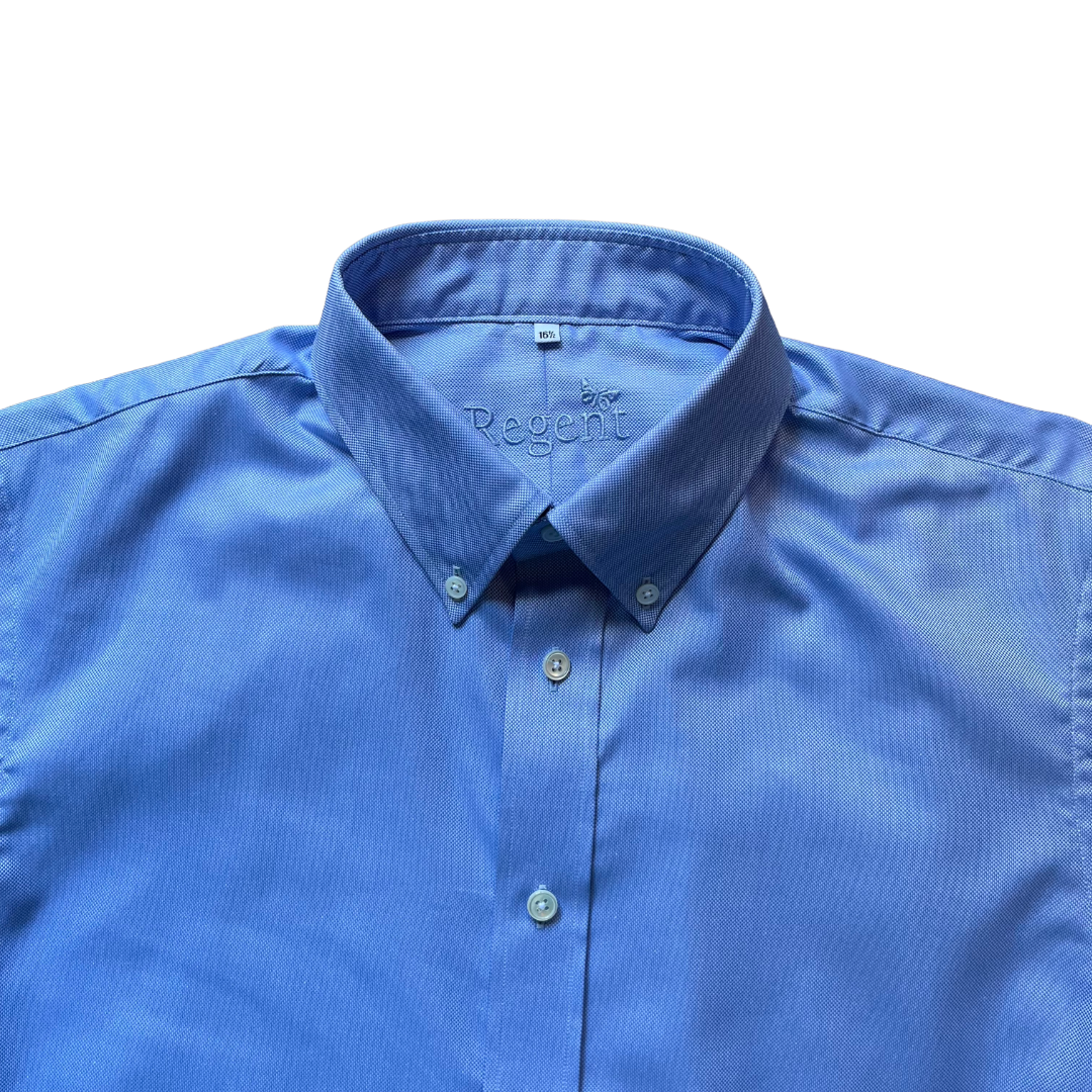 A close-up of a blue button-down shirt with a pointed collar and matching buttons, laid . The inner neck label shows the brand name 'Regent'.