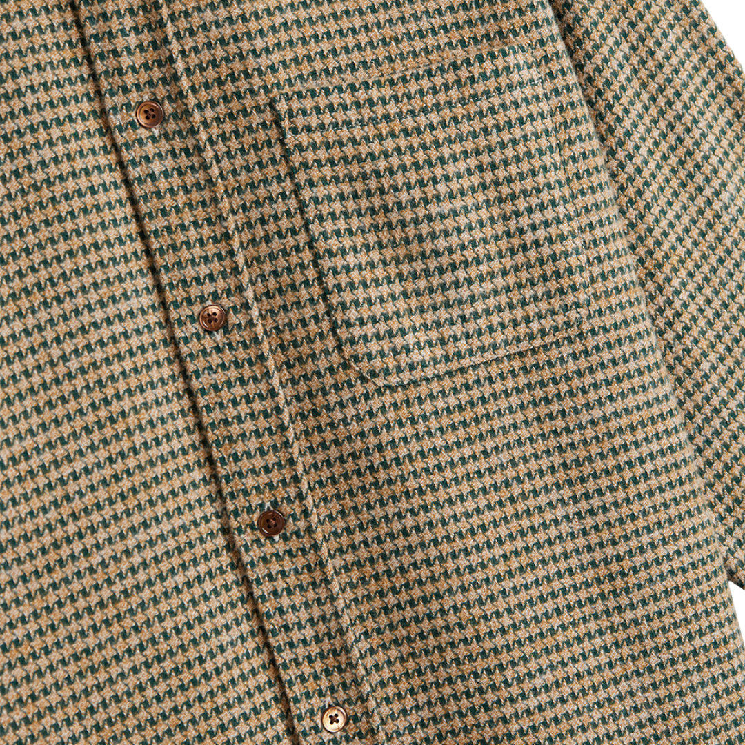 Close-up of a textured houndstooth patterned fabric in beige and dark green, featuring brown buttons down the front placket.