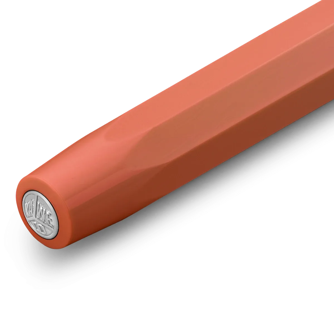 A close-up of a smooth, matte orange-brown cylindrical product, likely a pen or stylus, showing a silver circular logo stamp on the end cap against a clean white background.