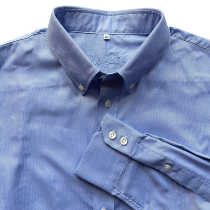 A close-up of a blue long-sleeve dress shirt with a spread collar and folded cuff, showing the button placket and inner neck label.
