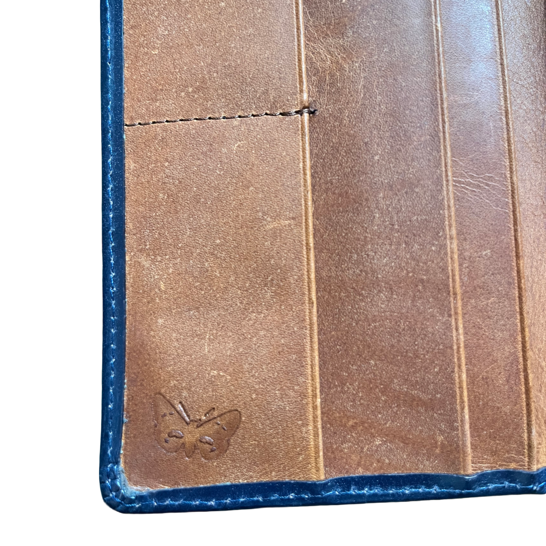 Close-up of a brown leather wallet or card holder showing the interior side with blue stitched edges and a small embossed butterfly logo near the bottom left.