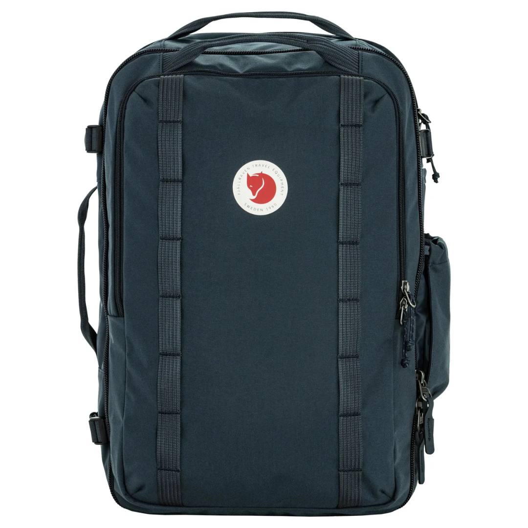A Fjälken backpack in dark navy blue, featuring a vertical zippered front pocket with a classic red fox logo patch on the front, set against a plain white background.